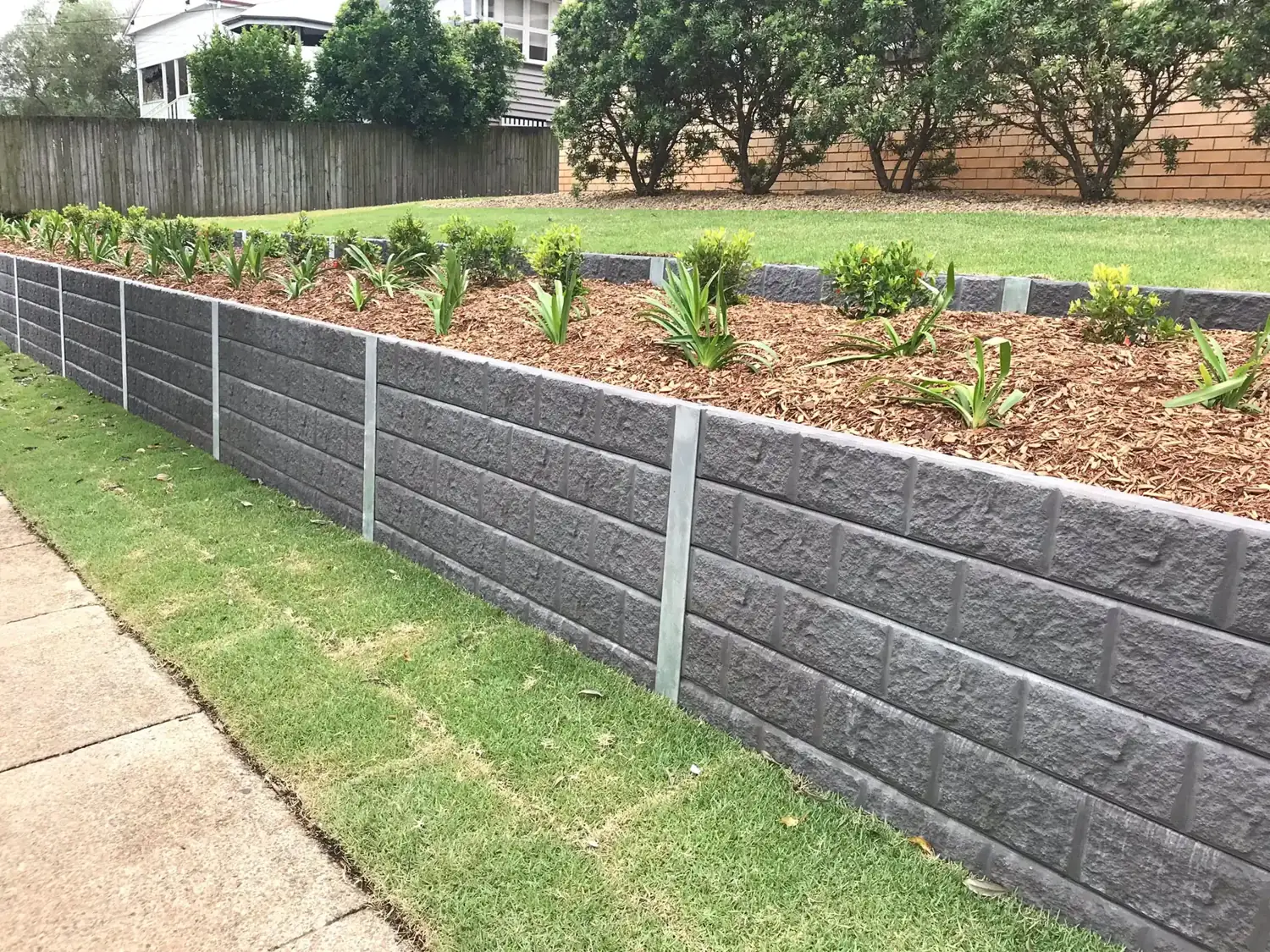 Grey textured concrete sleeper retaining wall holding a planted garden bed beside a lawn