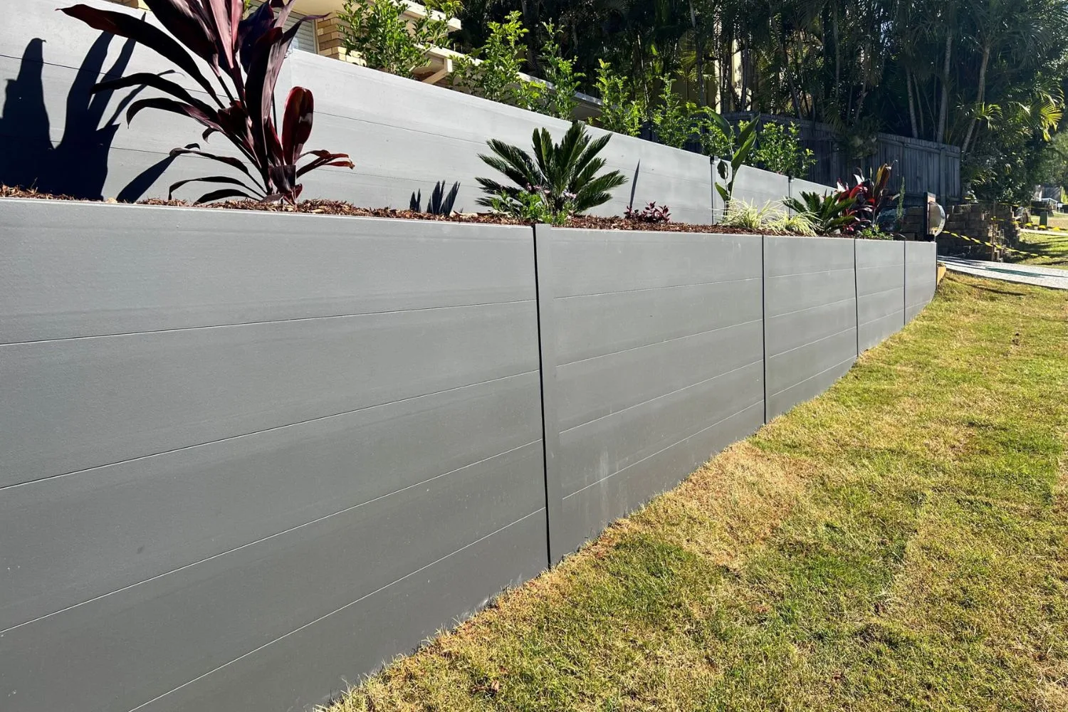 Long grey concrete retaining wall beside a lawn and garden