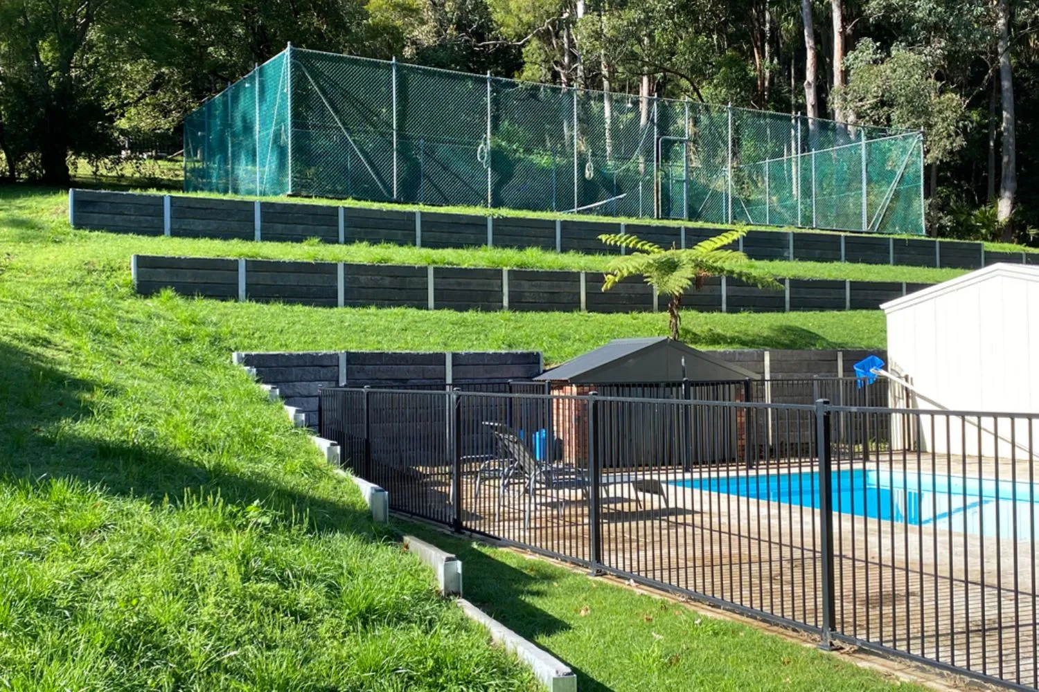 Tiered concrete sleeper retaining walls stepping down a sloped yard beside a pool