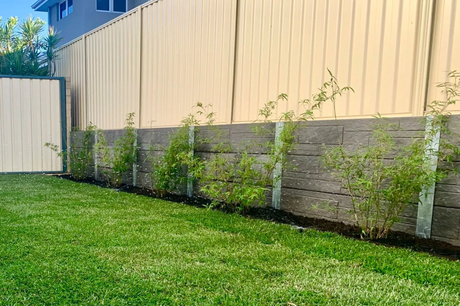 Concrete sleeper retaining wall with new plants below a colorbond fence
