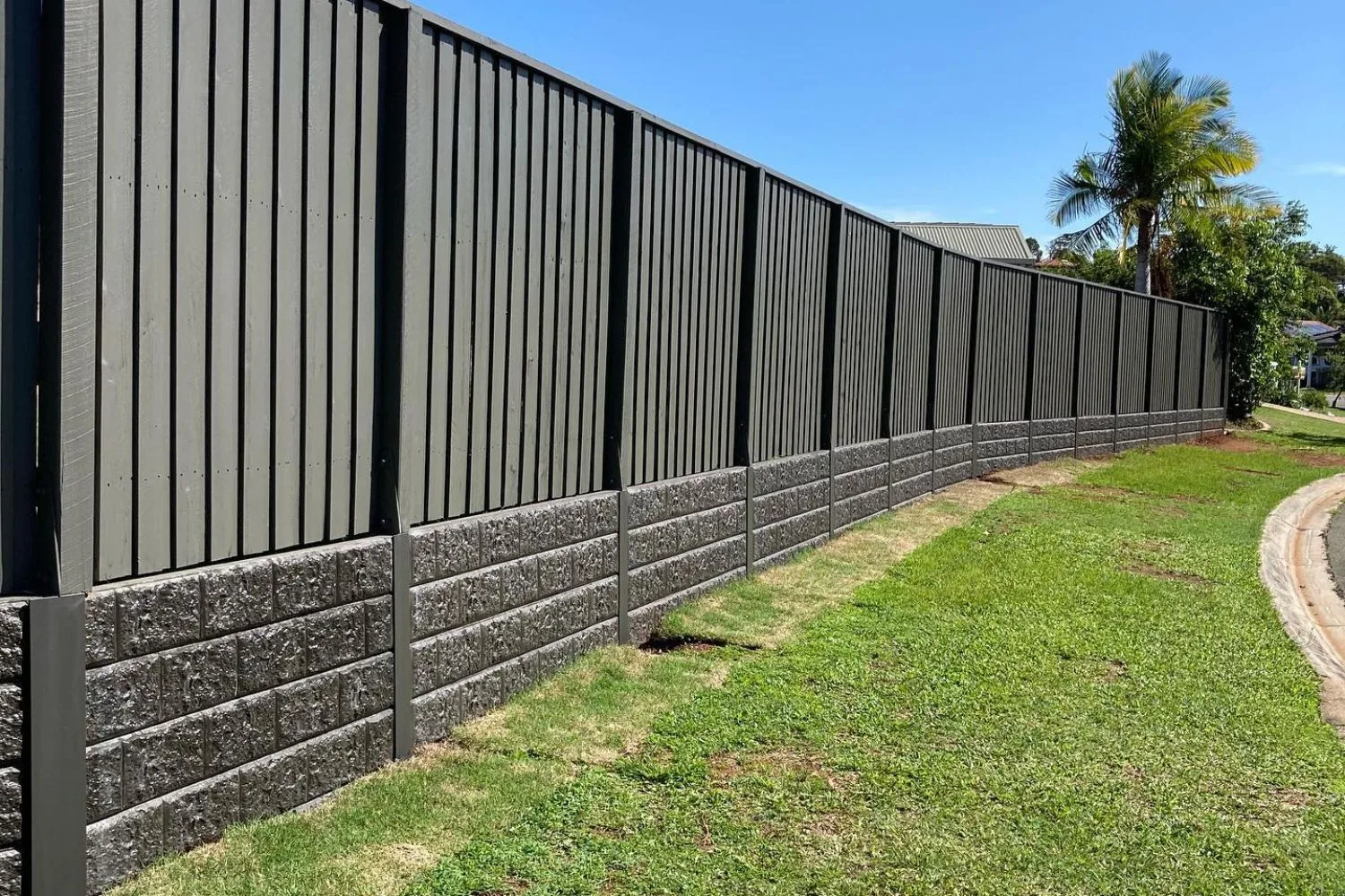 Dark concrete sleeper retaining wall beneath a black fence line