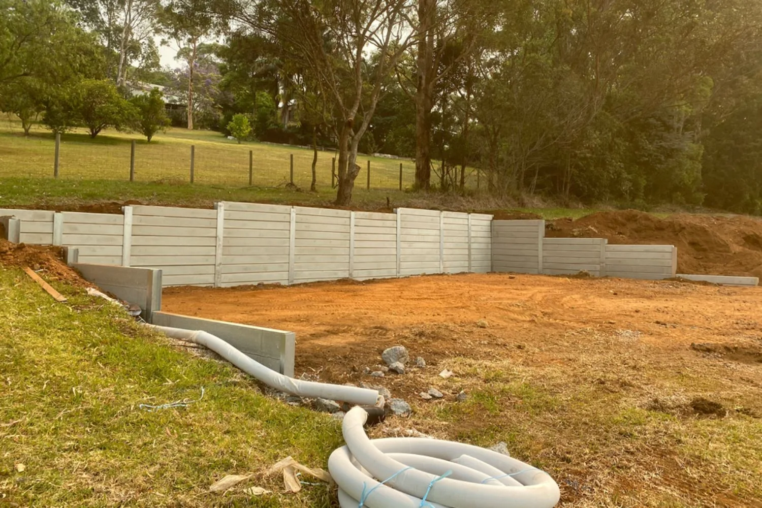 Concrete sleeper retaining wall being installed with drainage pipe on site