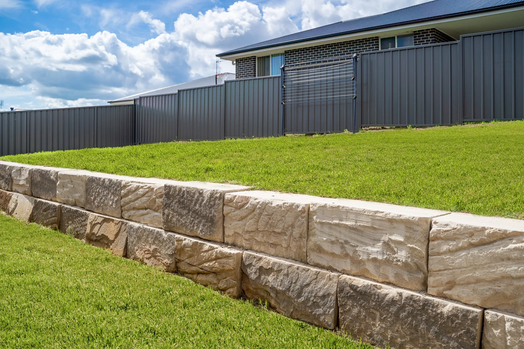 Sandstone block retaining wall edging a lawn below a fence