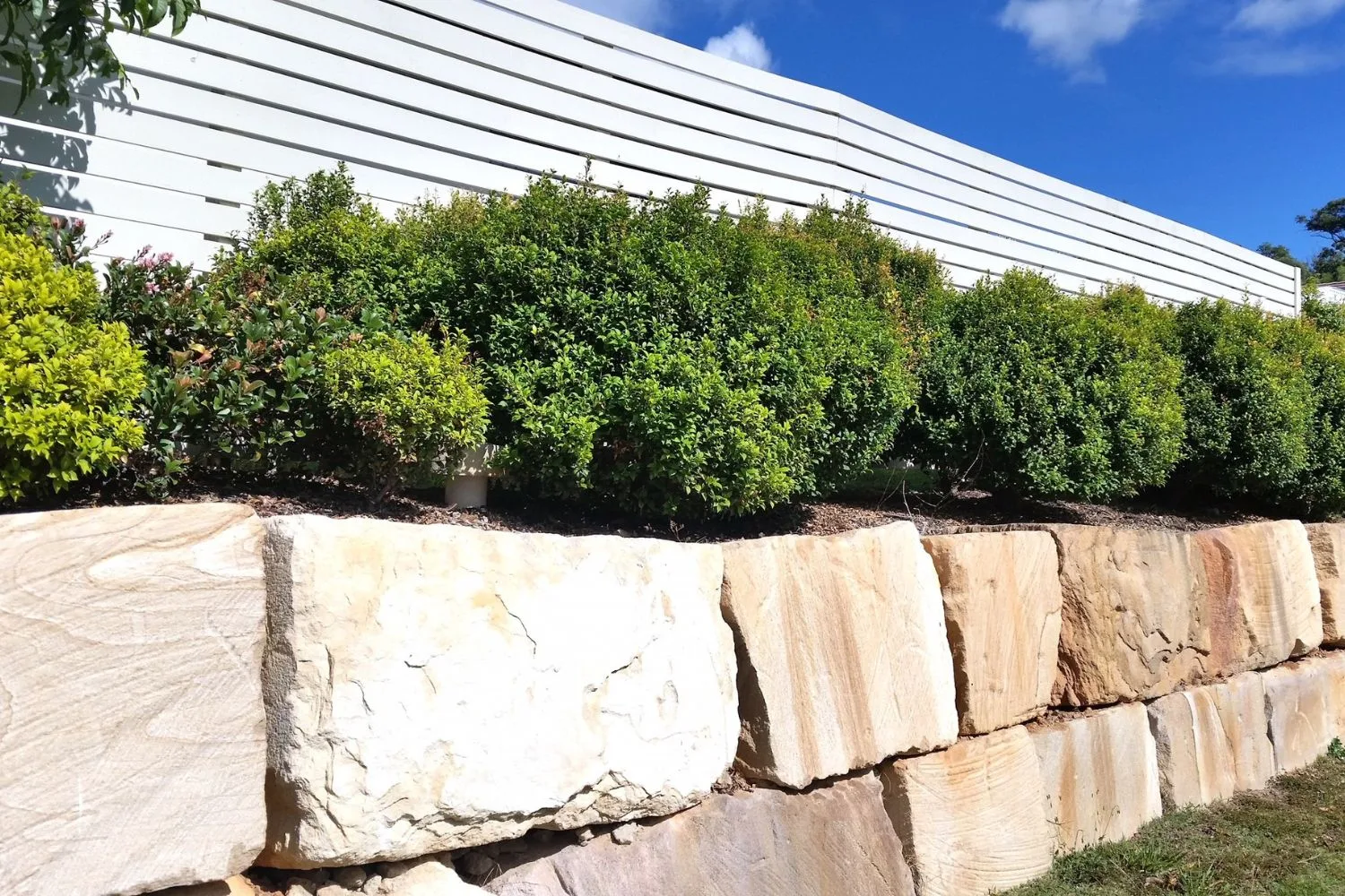 Large sandstone boulder retaining wall supporting a garden bed