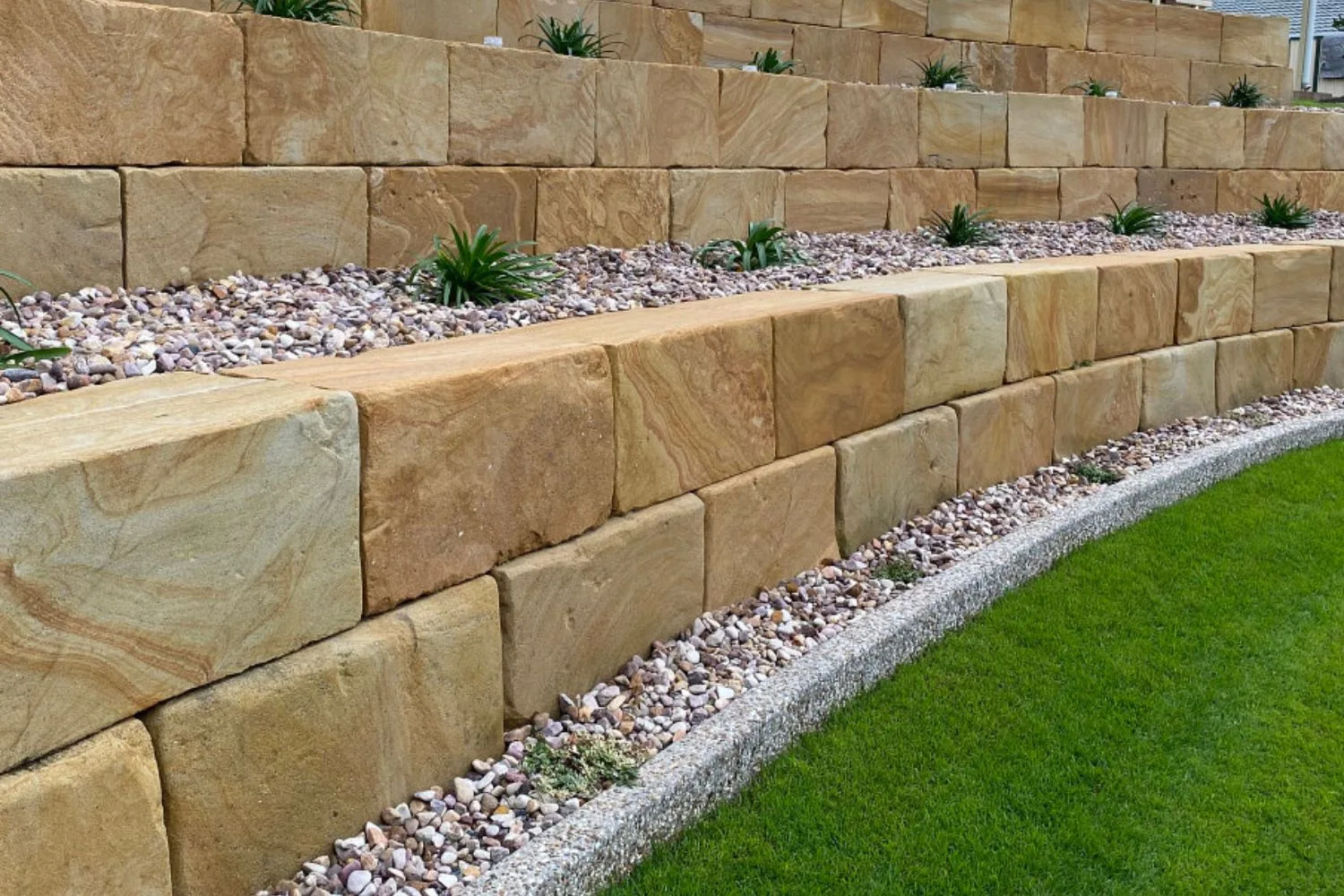Sawn sandstone block retaining wall above a lawn edged with gravel