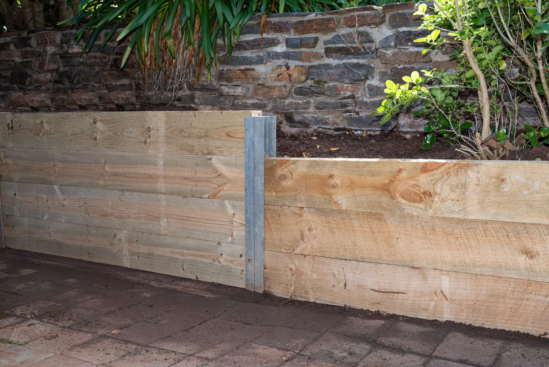 Timber sleeper retaining wall with galvanised posts beside paving